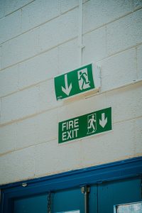 snapshot of green fire exit sign above blue door on white wal